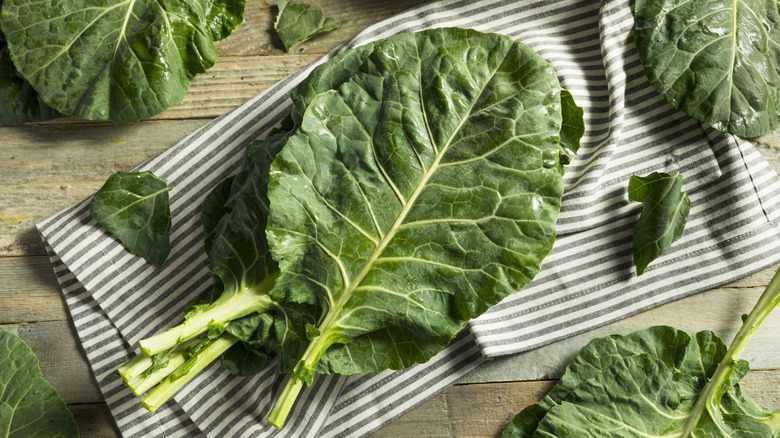 Raw collard greens on a striped cloth napkin on a wooden surface.