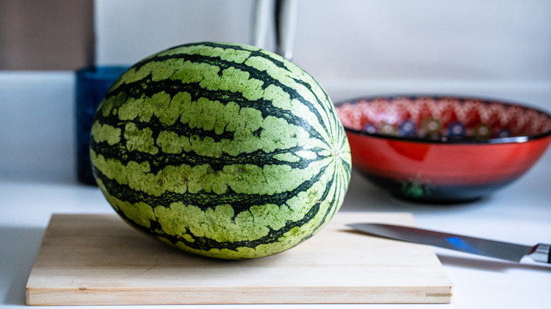 A whole watermelon and a big knife are arranged on a cutting board.
