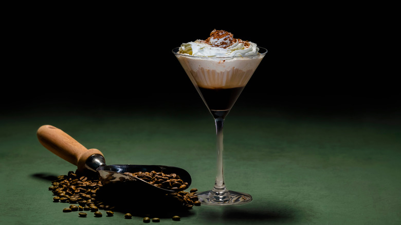 A whipped coffee martini and scoop of coffee beans against a green background