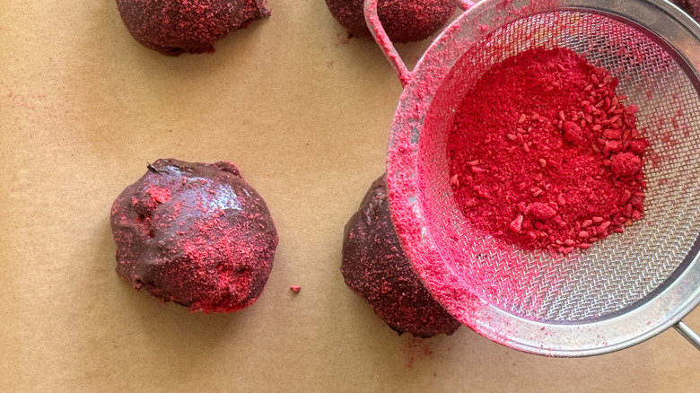 mesh strainer dusting raspberry powder onto truffles