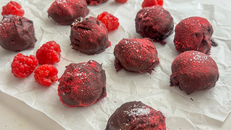 Raspberry chocolate truffles and fresh raspberries on parchment paper