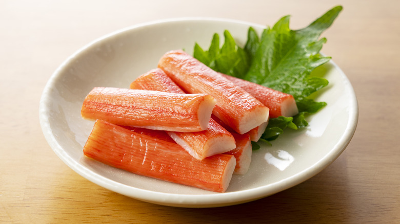Seven sticks of imitation crab meat on white plate with garnish