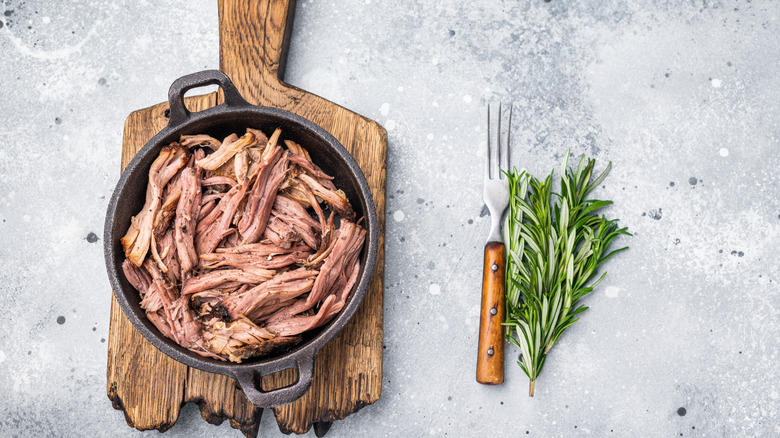 Shredded beef brisket in a cast iron pan on a rustic wooden cutting board