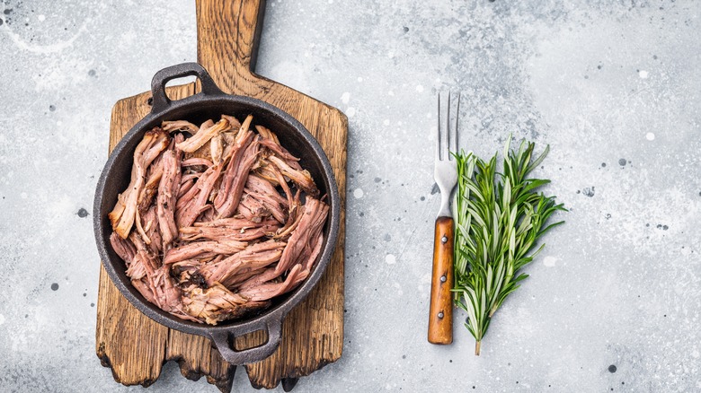 Shredded beef brisket in a cast iron pan on a rustic wooden cutting board