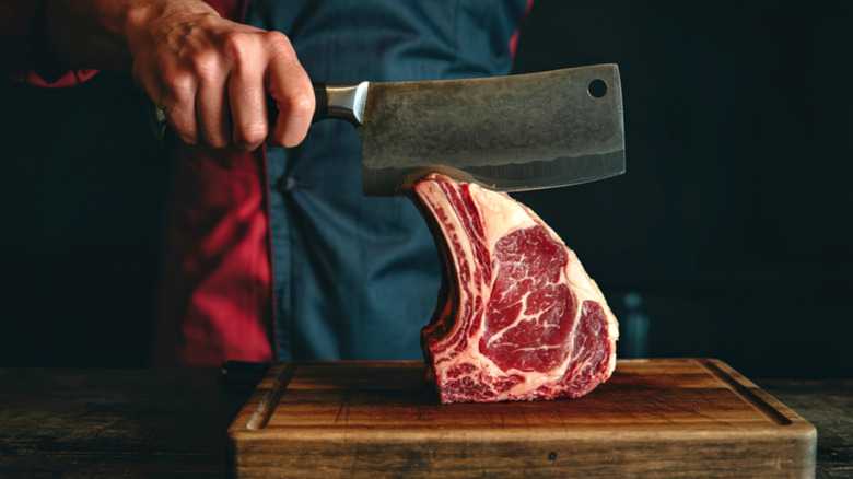 A hand using a butcher's knife to cut through a large piece of prime rib on a cutting board