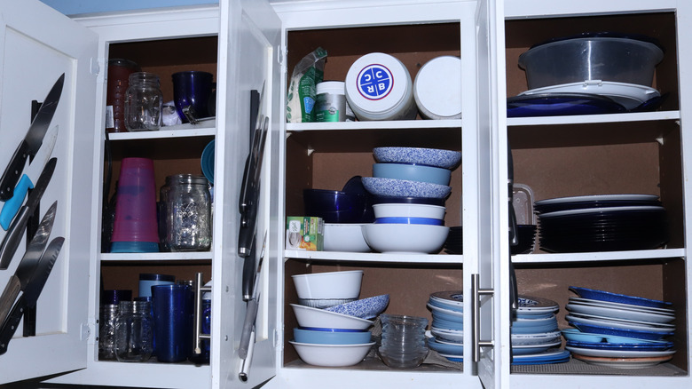cluttered kitchen cabinets with haphazardly stacked bowls and cups