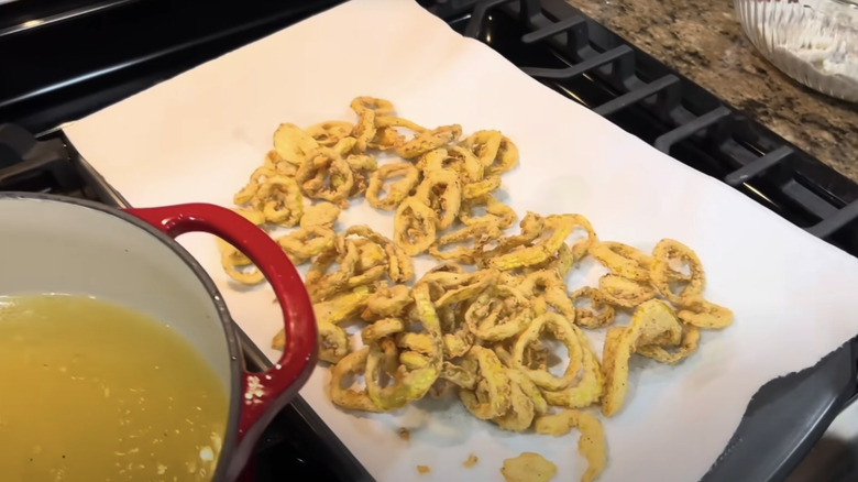 Deep-fried banana peppers on kitchen towel next to a red pot with oil