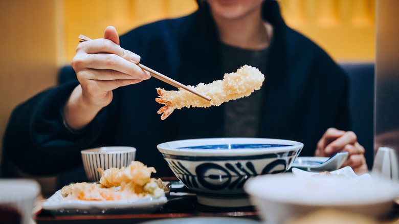 Hand holding shrimp tempura with a pair of chopsticks
