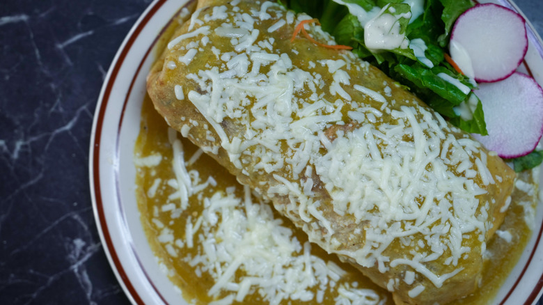 A burrito is smothered with green chili and topped with cheese