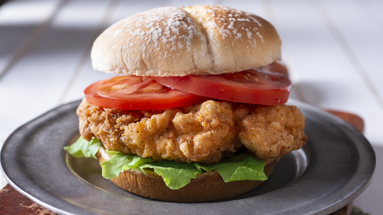a thick, fried chicken sandwich with tomatoes and lettuce on a sourdough bun
