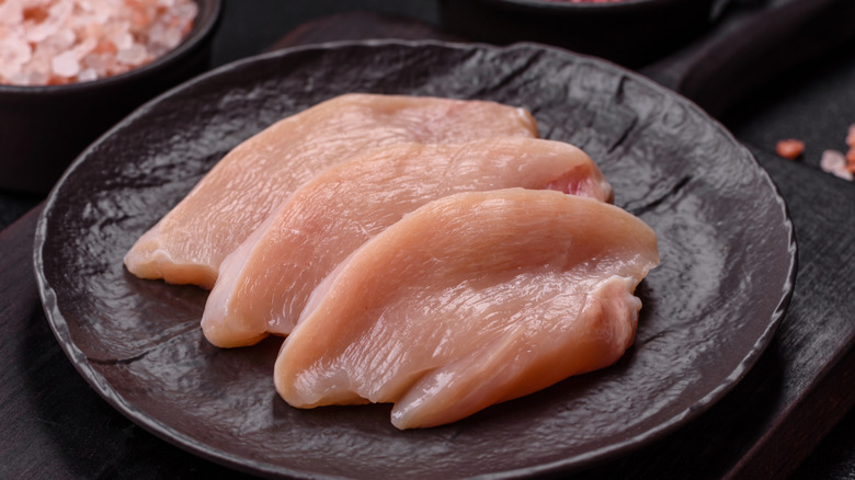 Sliced raw chicken breast on a brown plate.