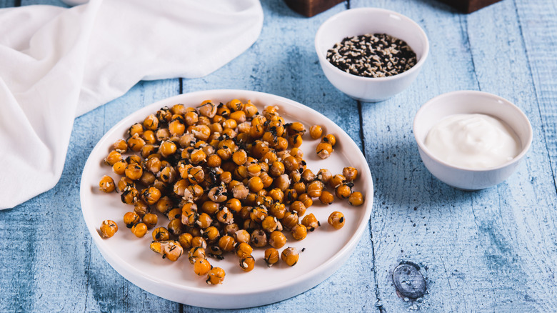 a plate of roasted chickpeas with sesame seeds and herbs on a wooden table