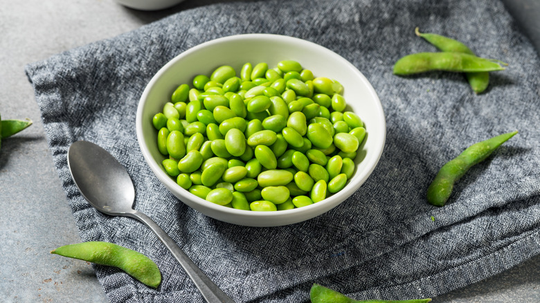 a bowl of edamame on a gray cloth napkin alongside a spoon