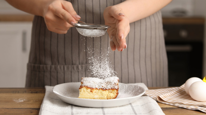 Person sprinkling powdered sugar on a cake