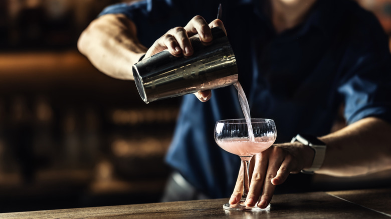 bartender pouring Cosmopolitan into coupe glass