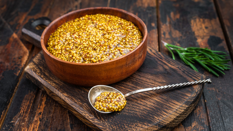 mustard with grainy texture in wooden bowl flat lay on wooden background with copy space.