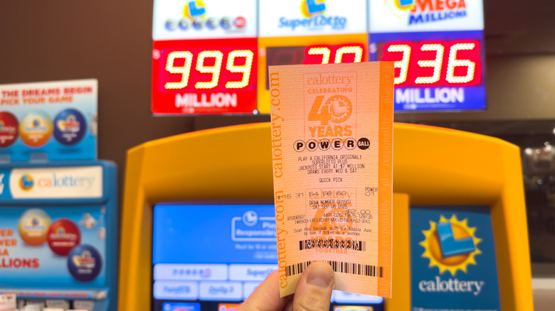 Someone holding a Powerball lottery ticket with prize money winnings shown in the background