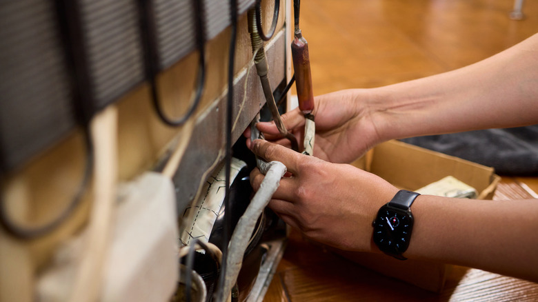 Person performing a repair on the back of a refrigerator