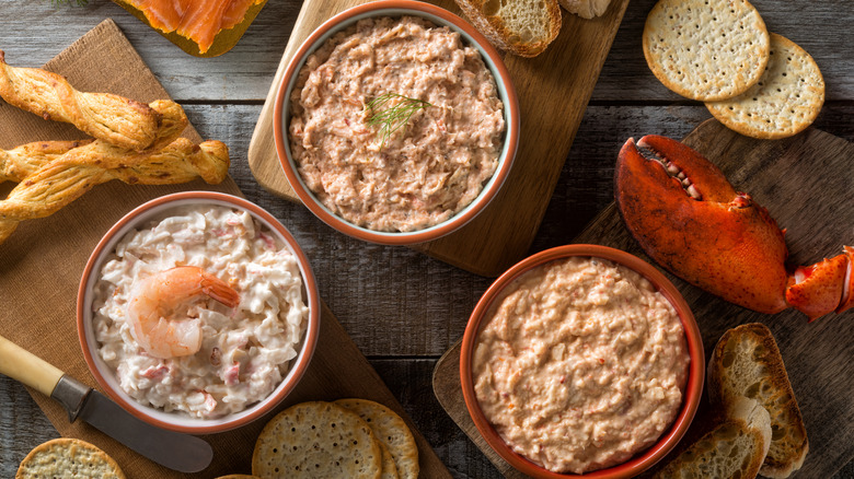 Seafood dips in bowls on cutting boards with crackers and a lobster claw