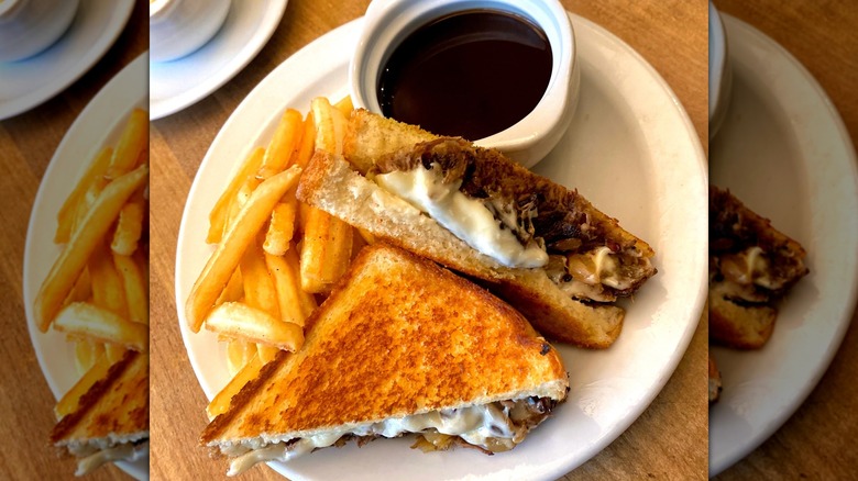 Top view of the Big Dipper Melt from Denny's, with two diagonally cut halves of a sandwich next to fries and a small bowl of au jus