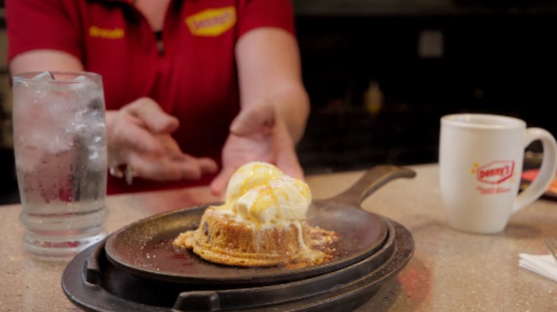 A waitperson places a skillet with a Denny's lava skillet cookie in it on a table
