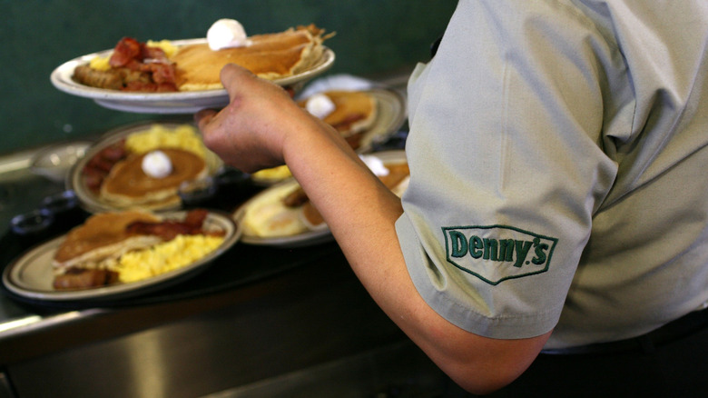 Plates of food at Denny's restaurant being picked up by the wait staff wearing a shirt with Denny's logo on sleeve