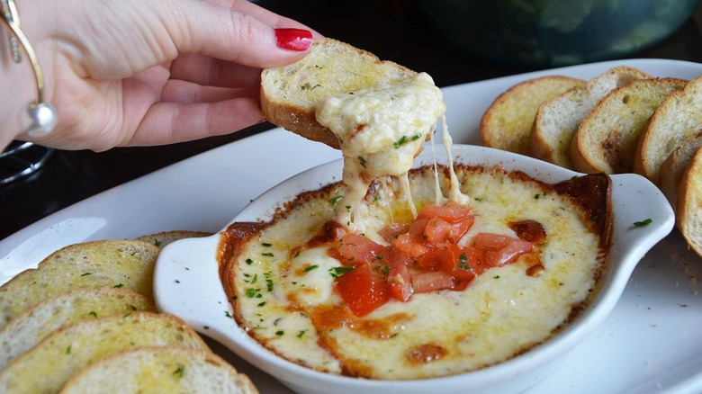 A person dipping bread in a bowl of Smoked Mozzarella Fonduta at Olive Garden
