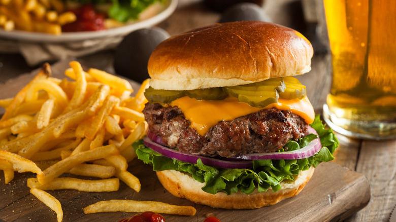 A cheeseburger with pickles, onions, and lettuce on a cutting board with a side of french fries