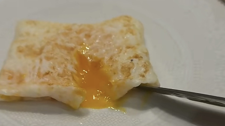 a knife cuts into the egg pocket and egg yolk spills out