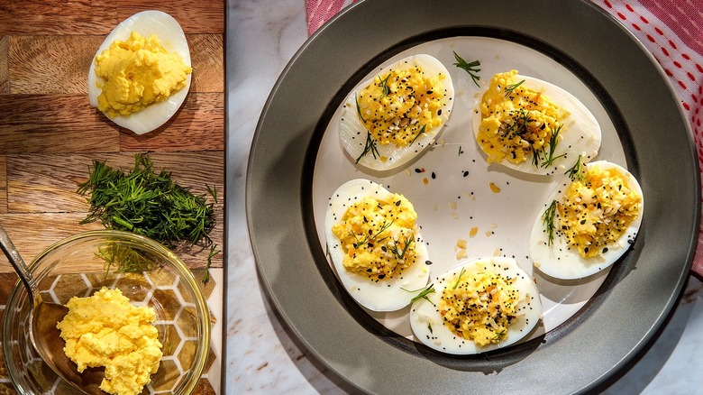 Deviled eggs with everything bagel seasoning and fresh dill on a white, gray, and black plate.