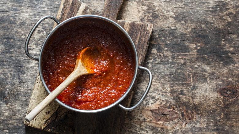 Pot of tomato sauce with wooden spoon on cutting board.