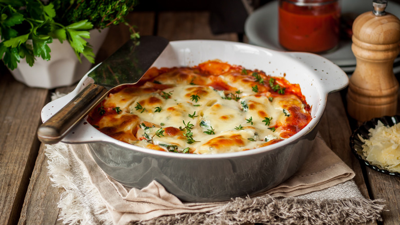 Individual-sized serving of lasagna in a circular crock with a serving spatula on a wooden table