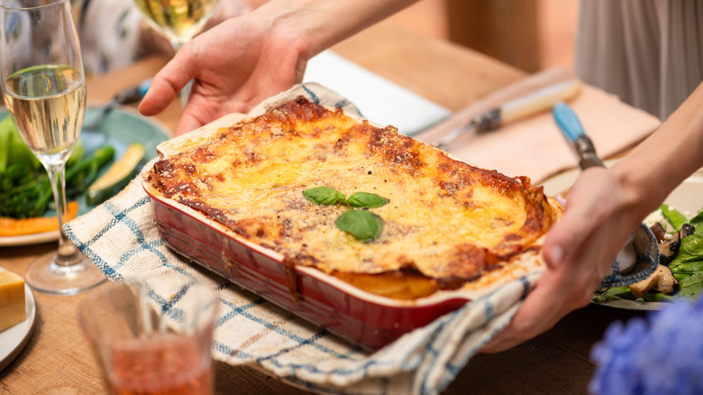 Person setting a pan of lasagna garnished with basil onto a set table