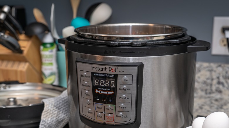 A sleek Instant Pot on a kitchen counter with knives and cooking tools in the background