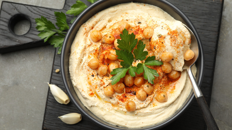 Delicious hummus with parsley, paprika, and chickpeas on grey table, top view
