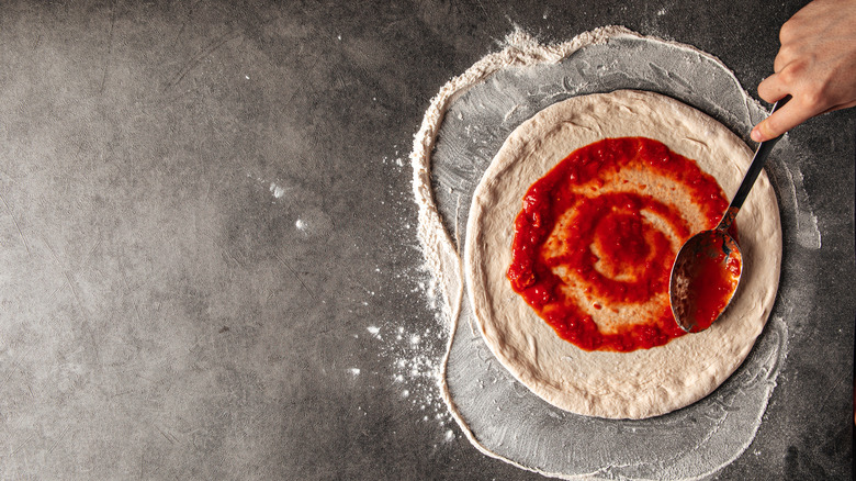 hand spreading tomato sauce on a pizza dough with a spoon