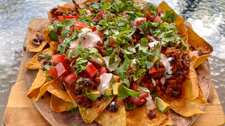 Loaded nachos piled high with chopped tomatoes, avocado, black olives, sour cream, and cilantro, served on a pizza stone.