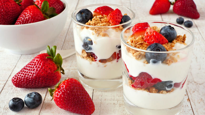 Yogurt parfaits with strawberries, blueberries, and granola surrounded by more berries