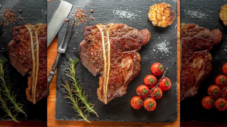 Grilled T-bone steak on a stone plate with garlic, herbs, tomatoes, salt, and seasoning
