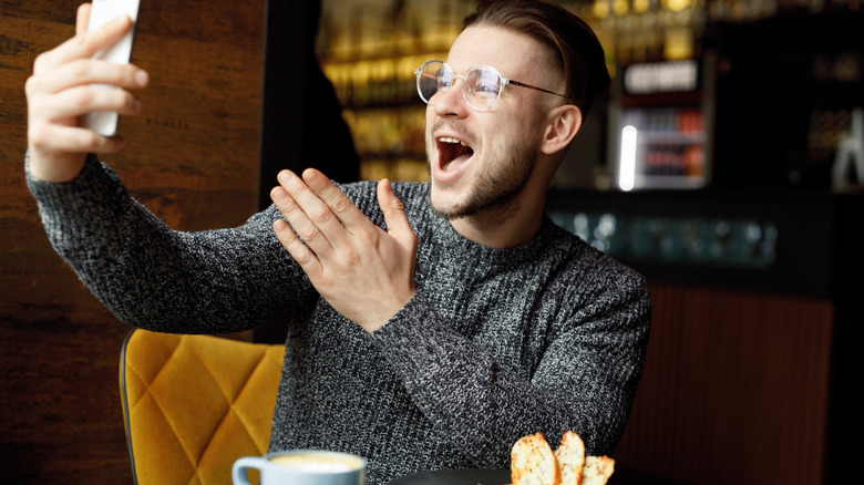 A person is making an exaggerated expression into their phone at a restaurant.