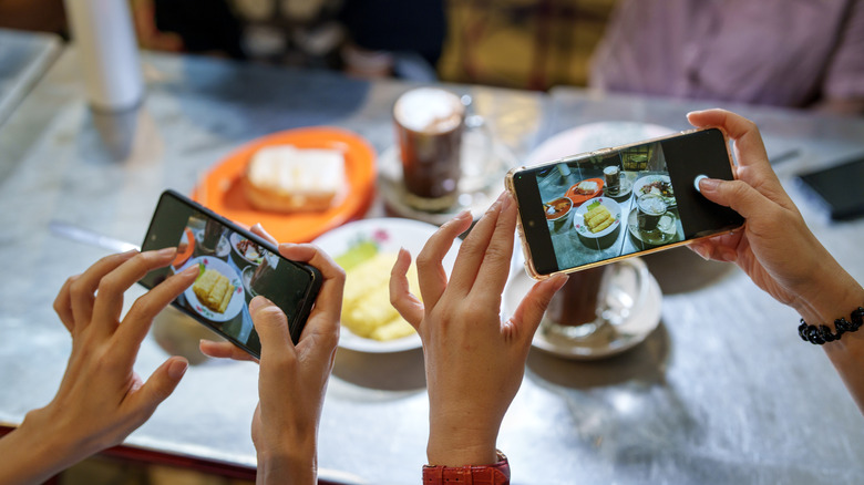 People's hands are seen making content with phones in a restaurant.