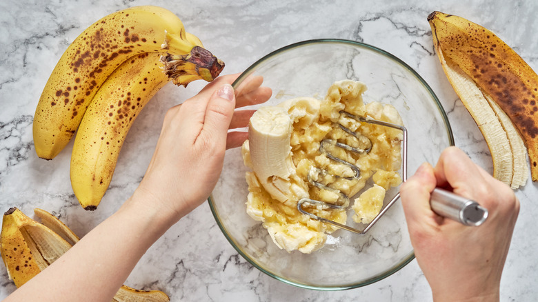 hands mashing bananas in bowl 