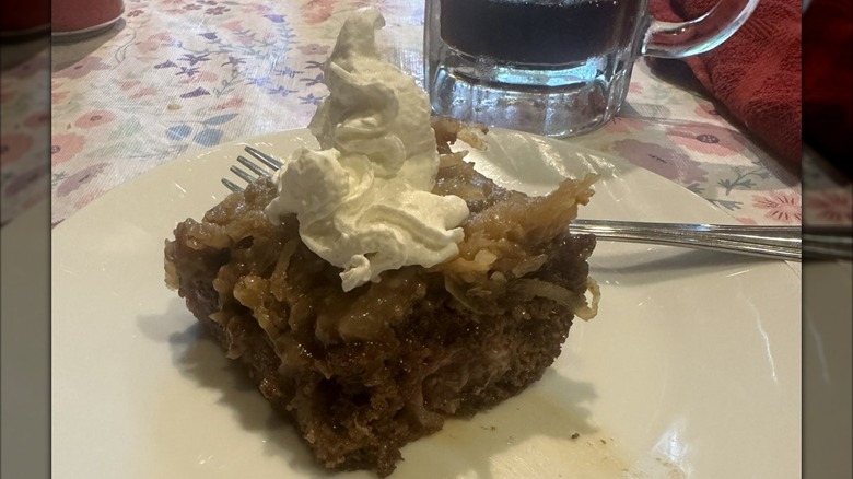 A square slice of Texas Tornado Cake topped with whipped cream on a white plate