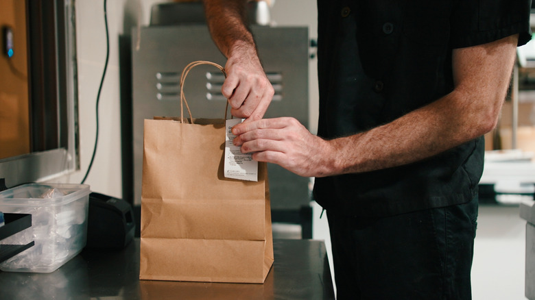 A person packing a takeout order in a brown paper bag.
