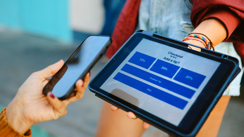 A person holding a tablet that shows a tipping prompt.
