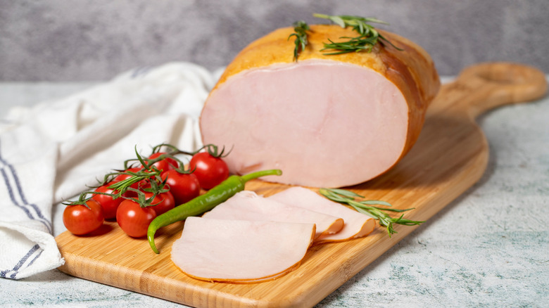 A large smoked turkey and cut slices for sandwiches are arranged with tomatoes on the vine on a cutting board.