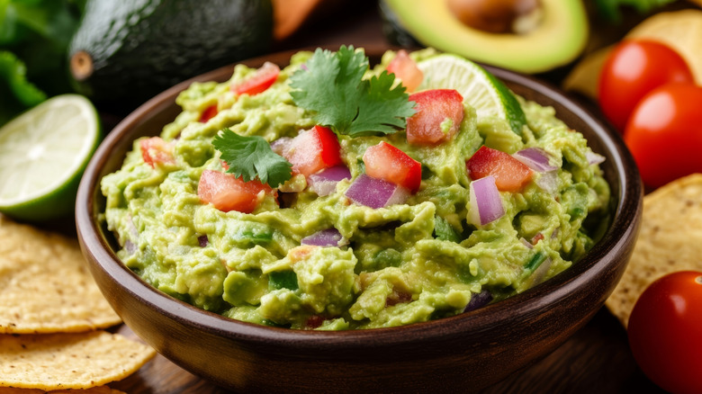 A bowl of creamy guacamole, garnished with tomatoes, onions, and cilantro.