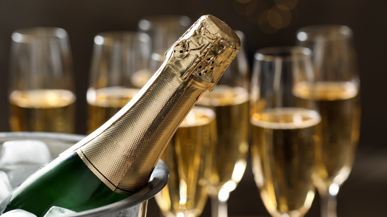 The neck of a bottle of champagne in an ice bucket, with filled flutes behind it.