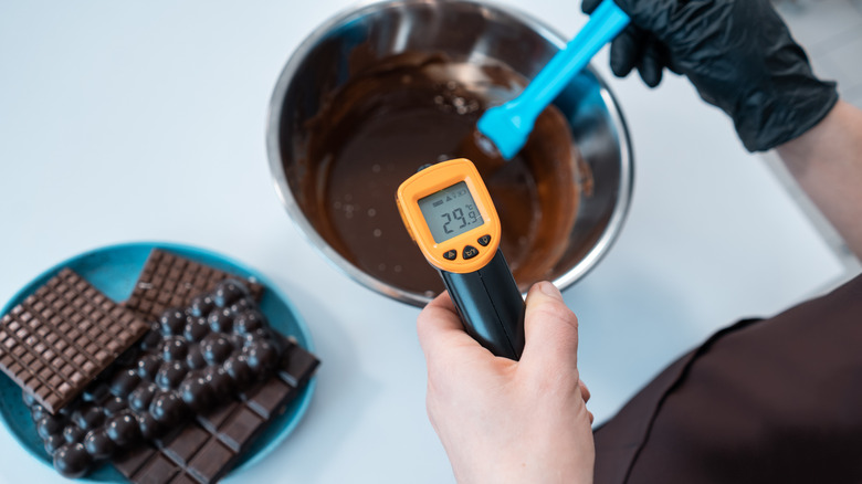 Hands using a candy thermometer for melted chocolate