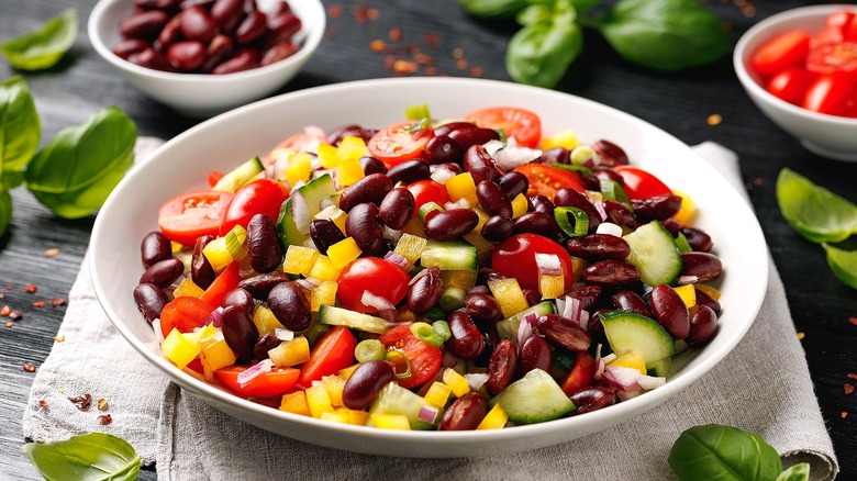 Kidney bean salad with chopped cucumbers, peppers, halved cherry tomatoes, and fresh basil in a shallow white bowl